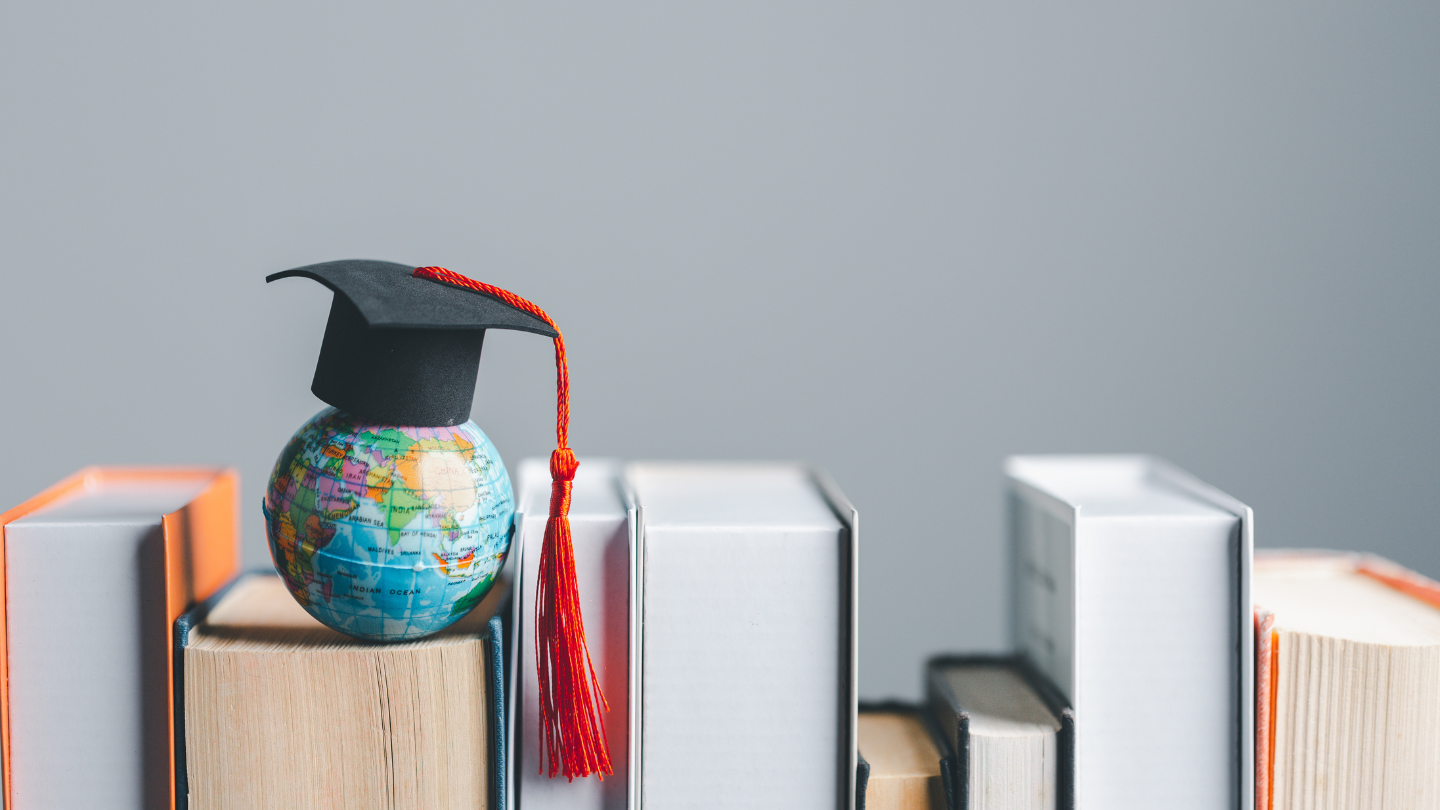 A small mortar board on top of a globe which is on top of books